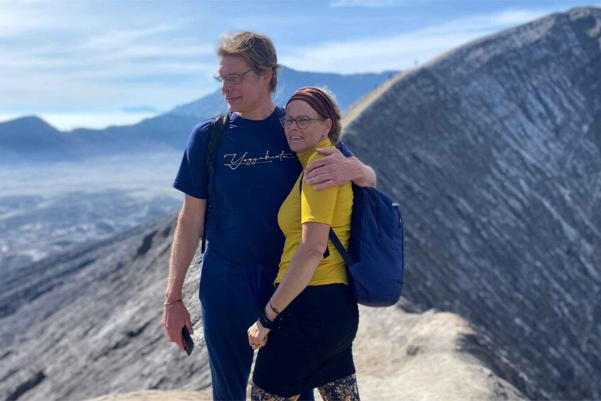 Two people standing on a mountain with a clear sky and distant mountains in the background. 3