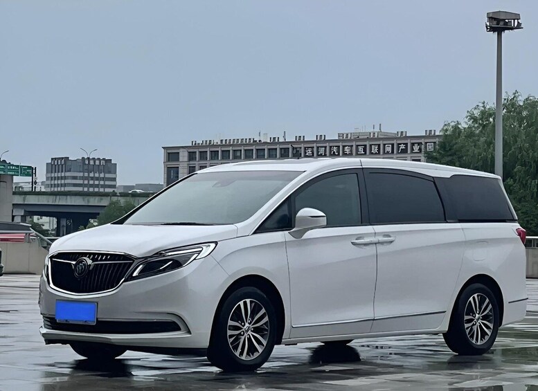 A white minivan parked on a wet surface with buildings and a streetlight in the background. 3