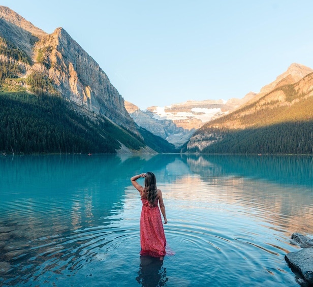 A woman in a red dress standing in a lake surrounded by mountains. 5