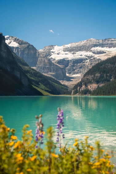 A mountain lake with clear turquoise water, surrounded by snow-capped peaks and dense forests. 2