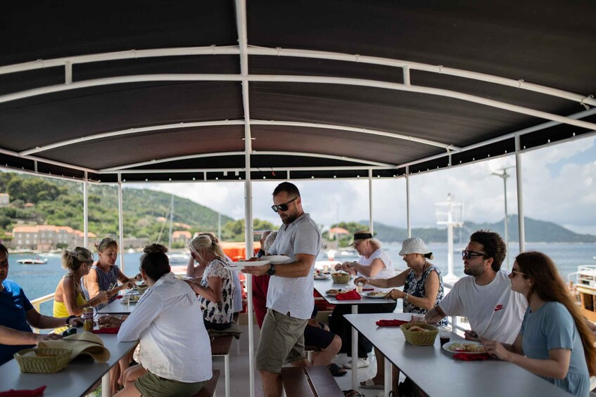 A group of people dining on a boat with a covered area and a scenic view of the water and hills in the background. 3