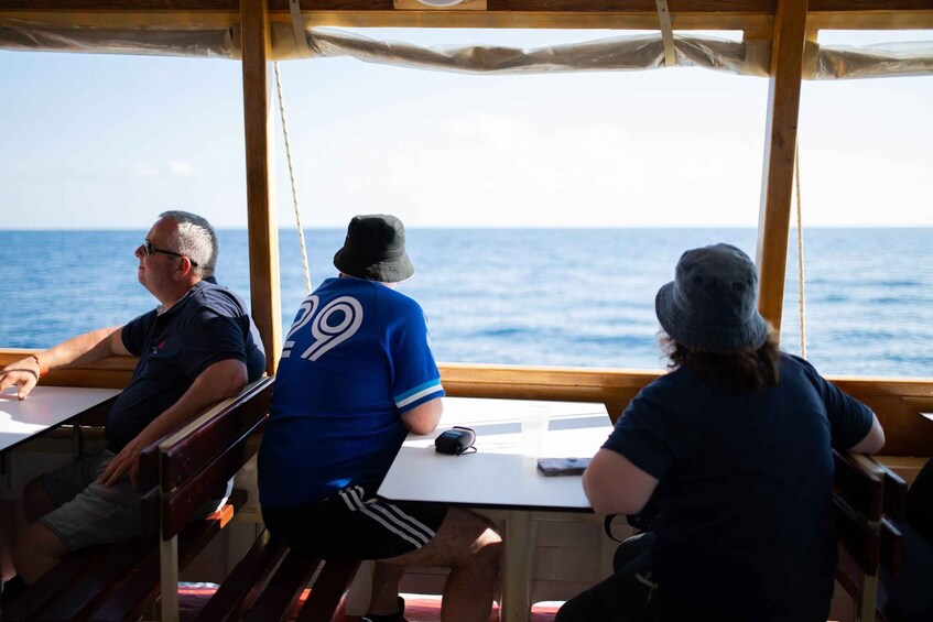 Three people seated at a table on a boat, looking out at the sea. 5