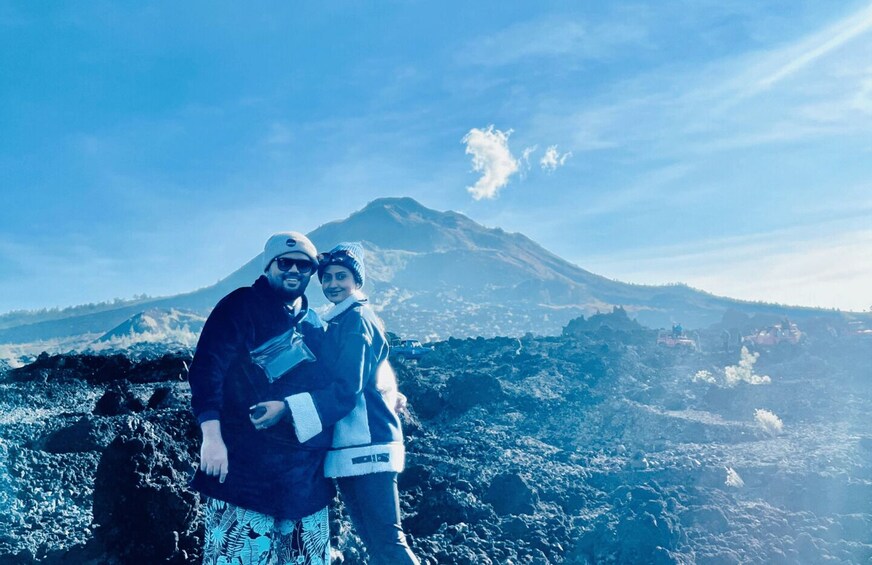 Two people standing on a rocky terrain with a mountain in the background. 1