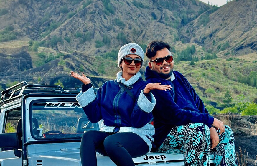 Two people sitting in a Jeep with a mountainous landscape in the background. 2