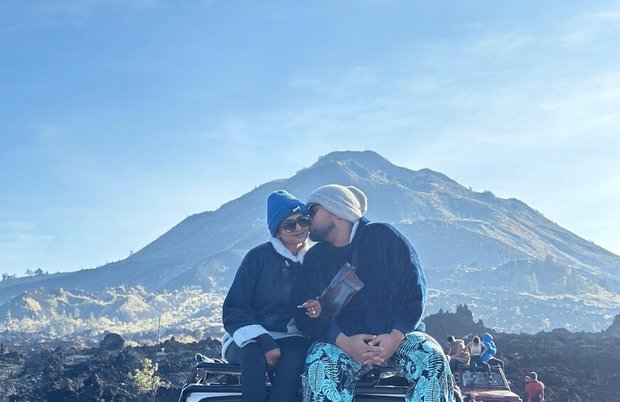 Two people sitting on a vehicle with a mountain in the background. 5