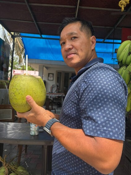 A person holding a green coconut with a straw. 5
