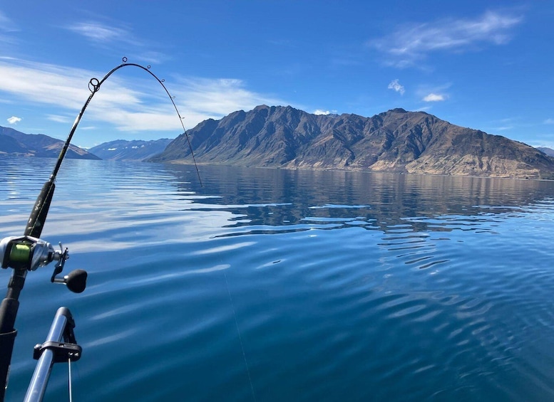 A fishing rod in the foreground with a calm lake and mountains in the background. 4