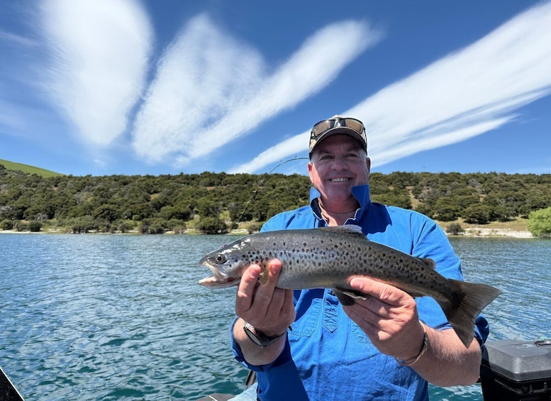 A person holding a fish on a boat with a lake and hills in the background. 2