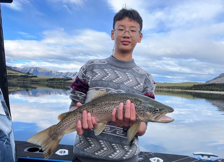 A person holding a fish on a boat with a mountainous landscape in the background. 3