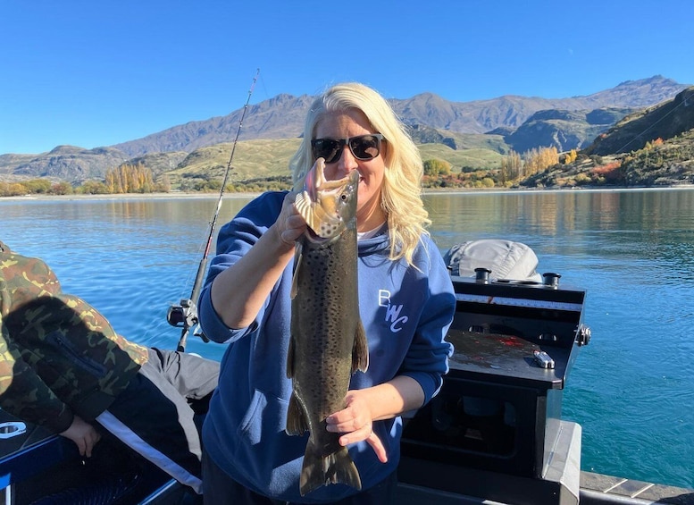 A person holding a fish on a boat with mountains in the background. 5