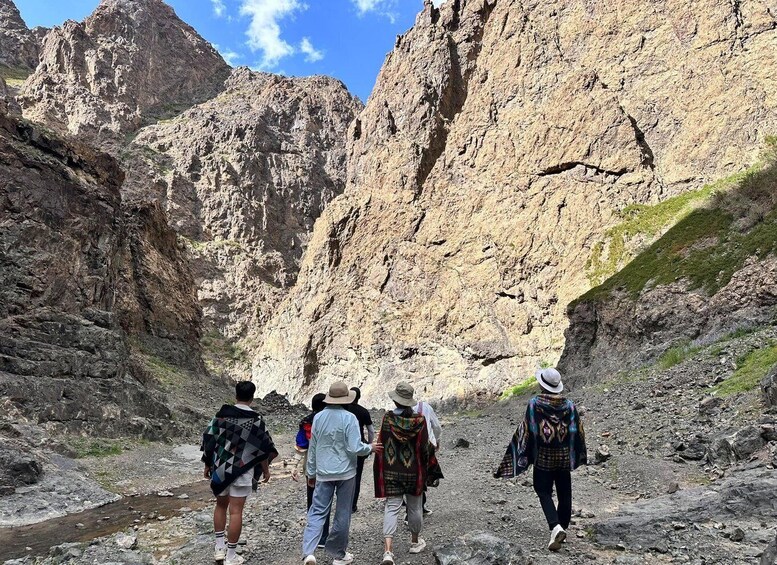 A group of hikers walking on a rocky trail with steep cliffs in the background. 2