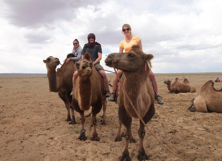 Three people riding camels in a desert. 3