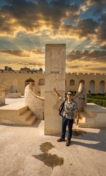 A person standing in front of a stone monument with inscriptions, pointing upwards, with a historical building in the background. 3