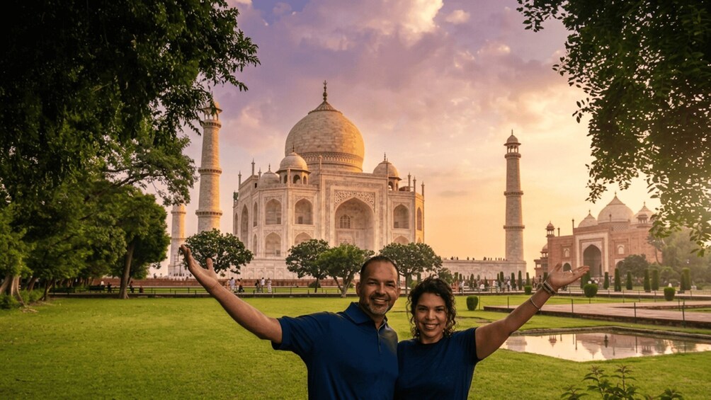 A couple with arms raised in front of the Taj Mahal, surrounded by greenery and a clear sky. 2