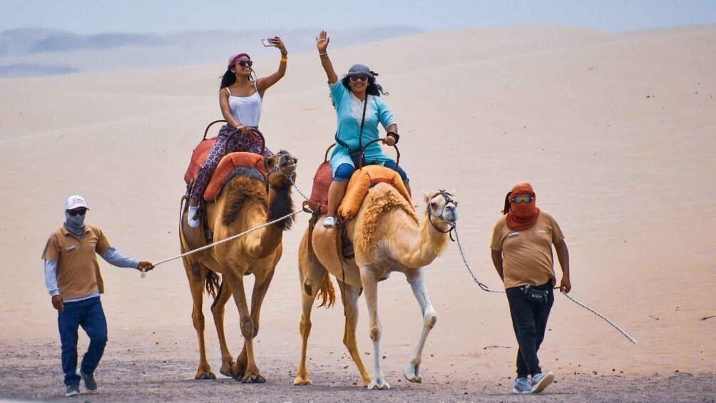 Three people riding camels in a desert. 1