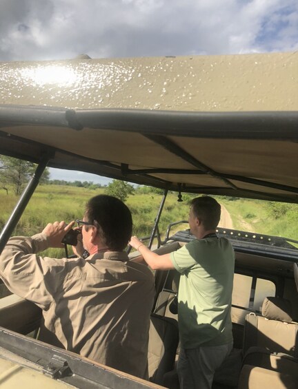 Two people inside a safari vehicle, one operating the vehicle and the other taking photographs. 1