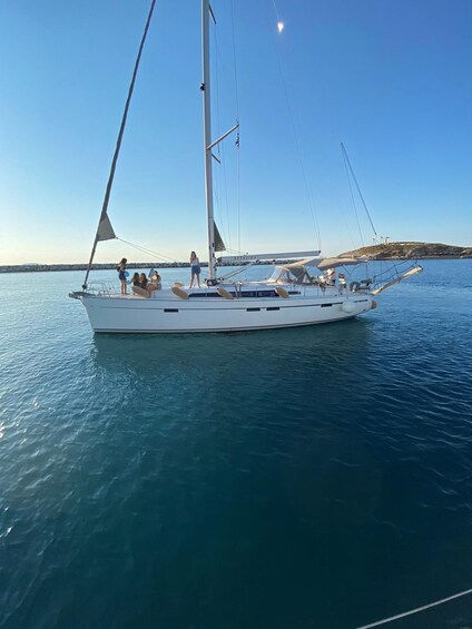 A white sailboat with people on deck, anchored in calm waters with a clear sky and distant land. 2