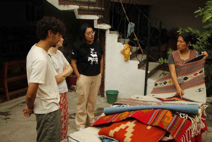 Three people standing outdoors near a staircase, with colorful blankets and a green bucket on the ground. 5