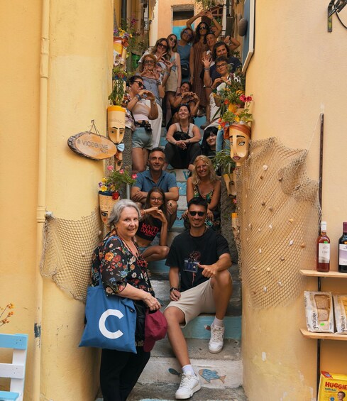 A group of people sitting on a narrow stairway with yellow walls, surrounded by potted plants and a decorative net. 2