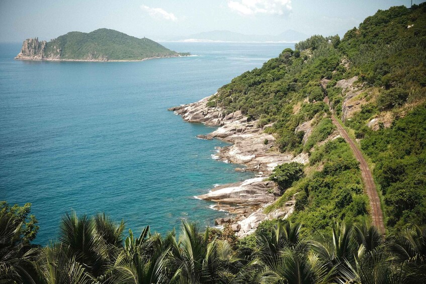 A coastal landscape with a rocky shoreline, dense greenery, and a distant island. 3