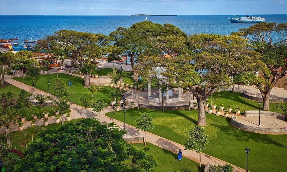 A coastal park with pathways, trees, and a distant ship. 1