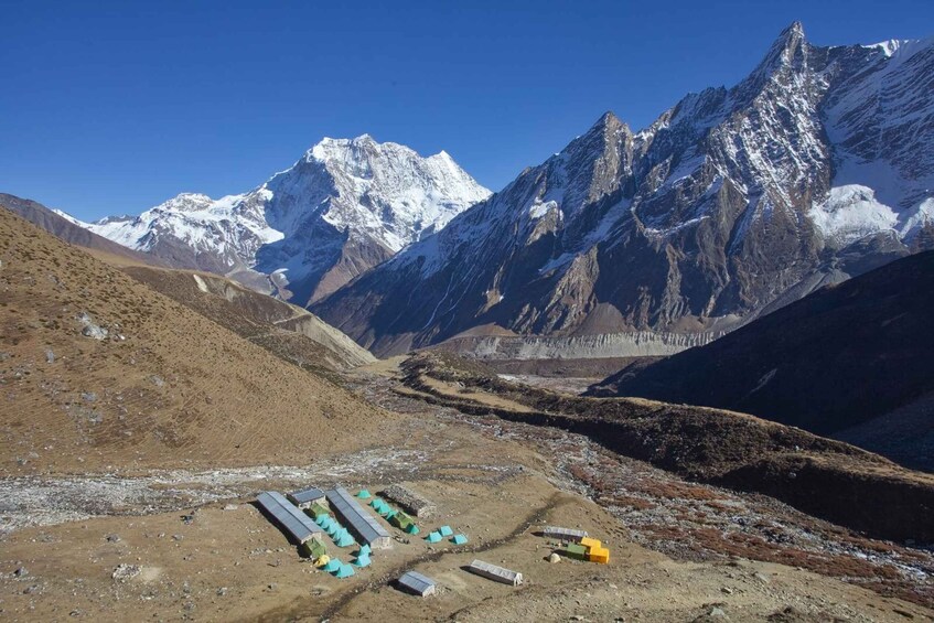 A mountainous landscape with snow-capped peaks and a valley with temporary structures. 1