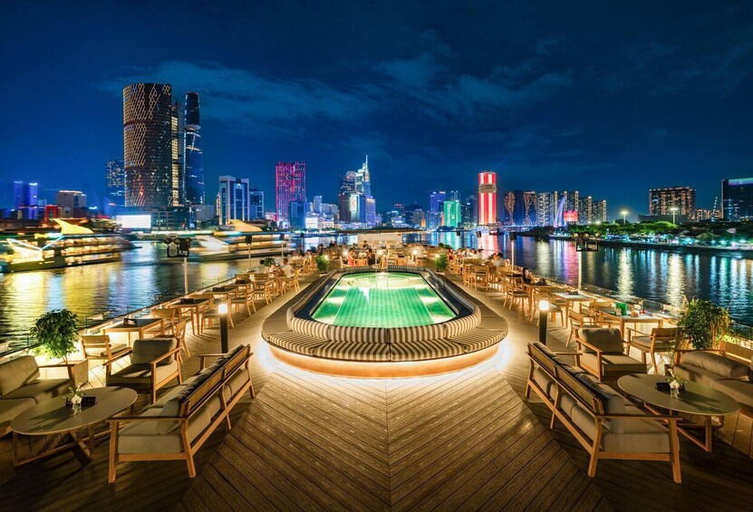 A waterfront deck with outdoor seating and a pool, overlooking a city skyline at night. 2