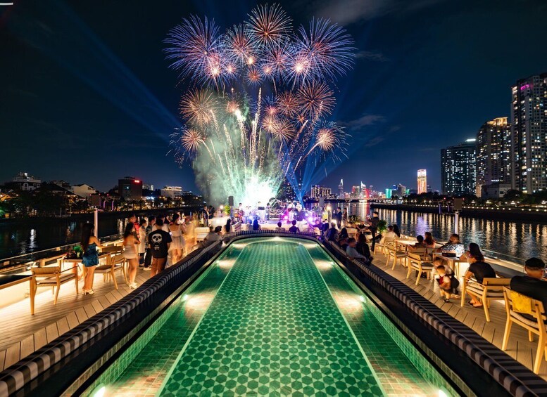 A nighttime waterfront with a pool, people dining, and fireworks in the sky. 5