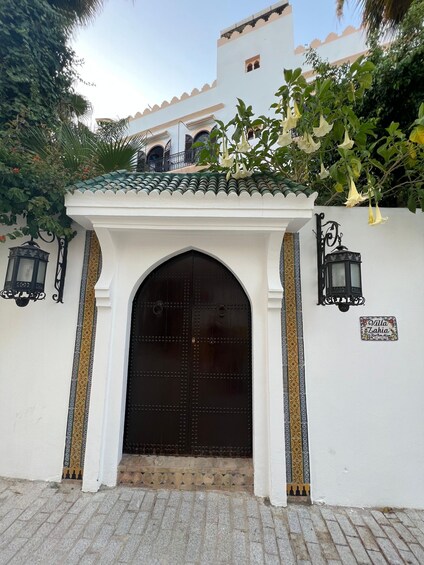 A white building with a large arched entrance, decorative tiles, and a sign reading "Villa Zahia." 3