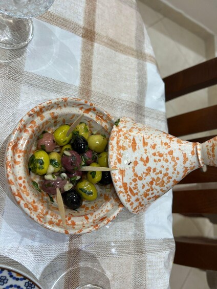 A bowl of olives and greens on a tablecloth. 5
