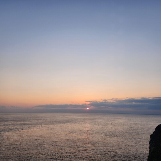 A sunset over a calm sea with a rocky coastline. 5