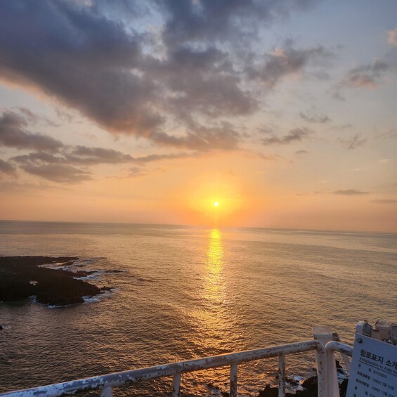 A sunset over the ocean with a railing in the foreground. 2