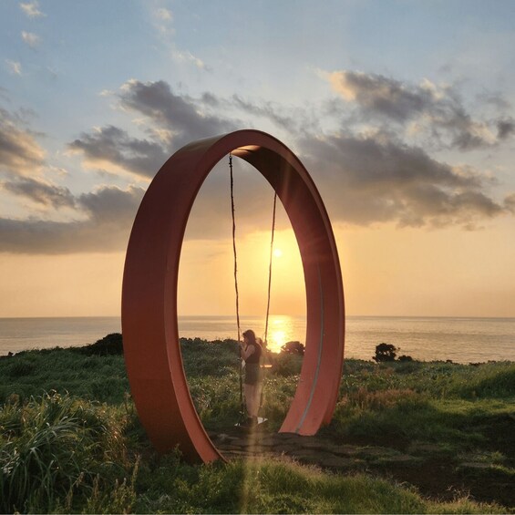 A person swinging on a large circular structure with a sunset in the background. 1