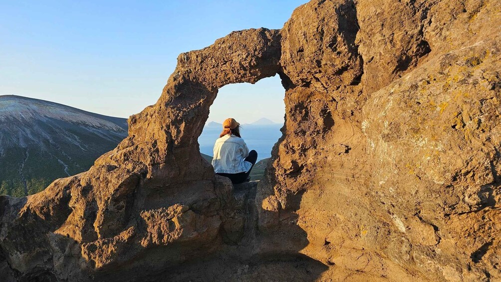 A person sitting inside a natural rock arch overlooking a mountainous landscape. 1