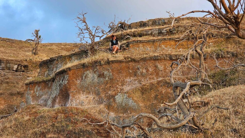 A person sitting on a rocky hillside with sparse vegetation and a clear sky. 3