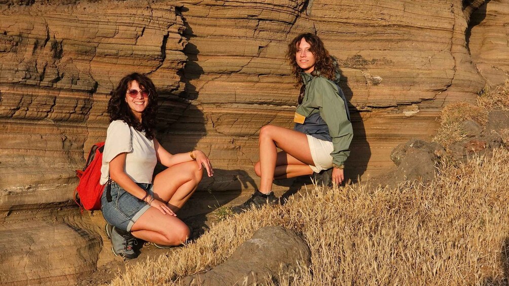 Two people sitting on rocks near a large rock formation. 4