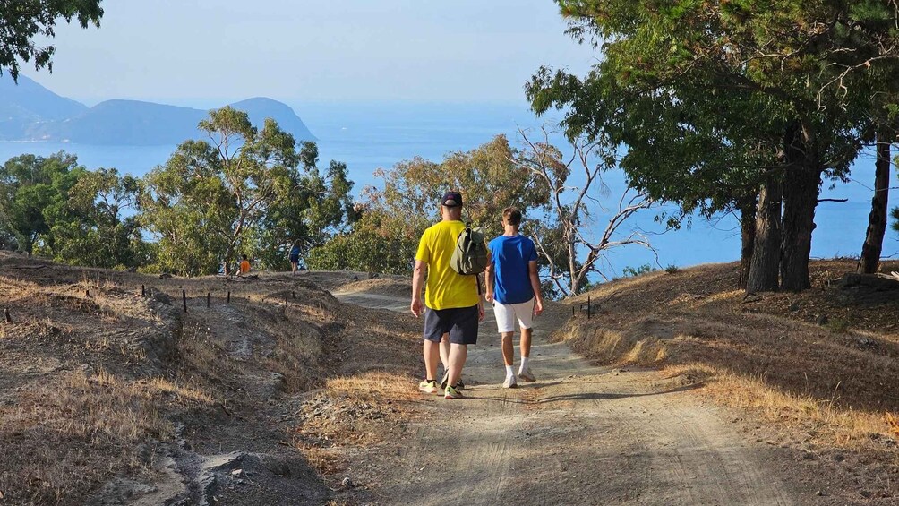 Two people walking on a dirt path surrounded by trees and a body of water in the background. 5