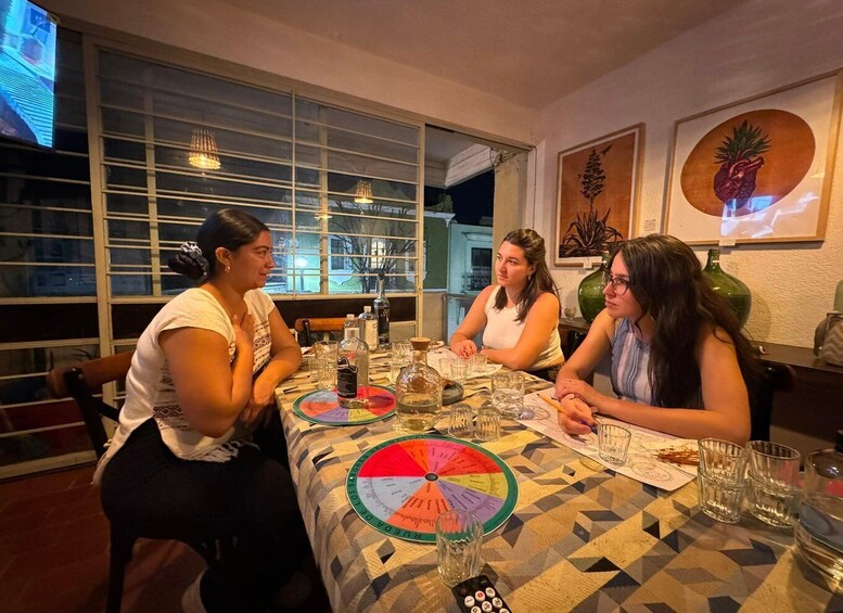 Three people sitting at a table with a colorful tablecloth, a remote control, and a glass of water. 1