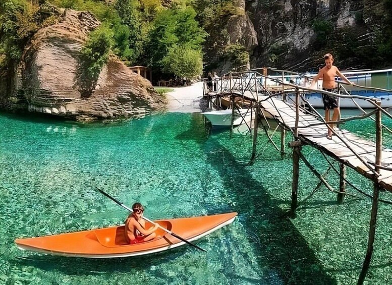 A person in a canoe on clear water, a wooden dock, and a rocky cliff. 2
