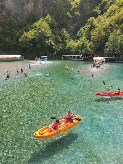 A group of people kayaking and swimming in a clear, turquoise lake surrounded by lush greenery. 5