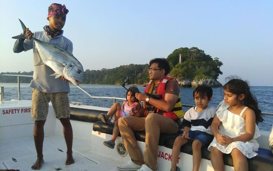 A boat with people fishing, a large fish held by a person, and a forested island in the background. 1