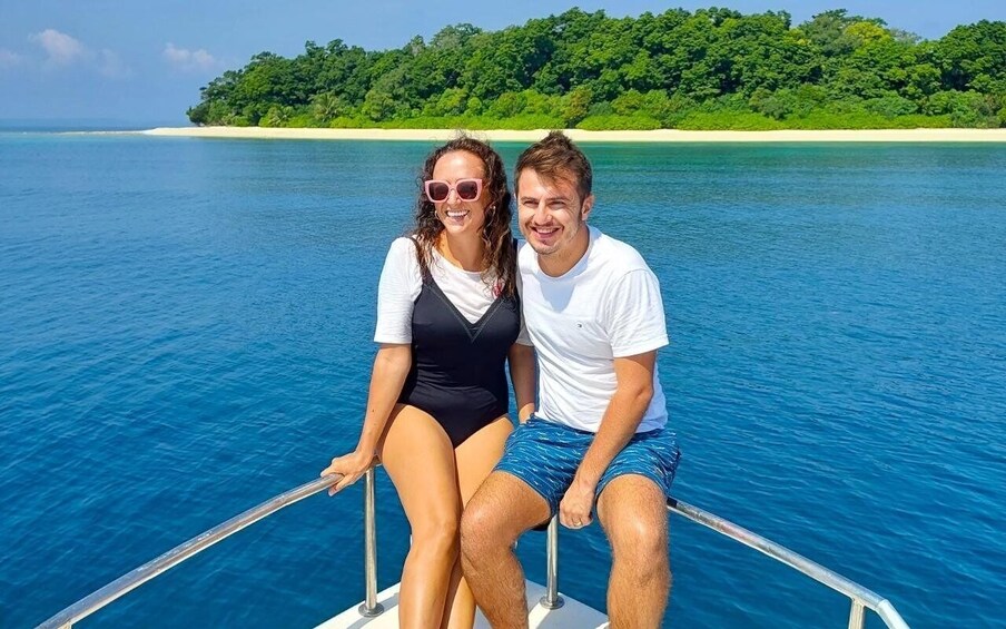 A couple on a boat with a clear blue sea and a green island in the background. 4