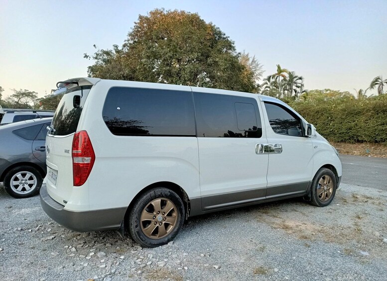 A white van parked on a gravel surface with trees and other vehicles in the background. 2