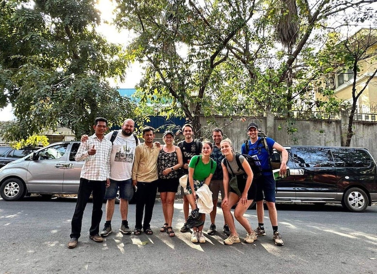 A group of people posing in front of parked cars and trees. 1