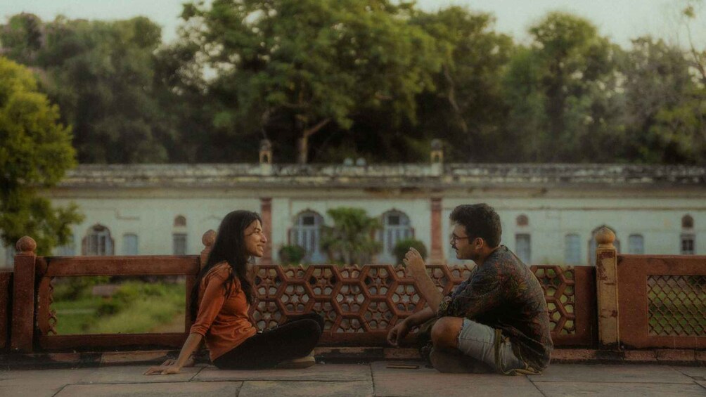 Two people sitting on a bench in a park with trees and a building in the background. 4