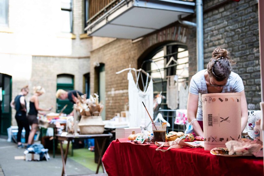 An outdoor market with tables covered in red cloths, various food items, and people engaged in activities. 5