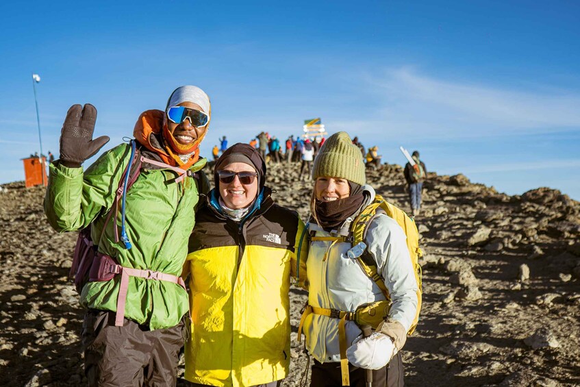 Three people in outdoor gear on a rocky terrain with a clear sky. 3