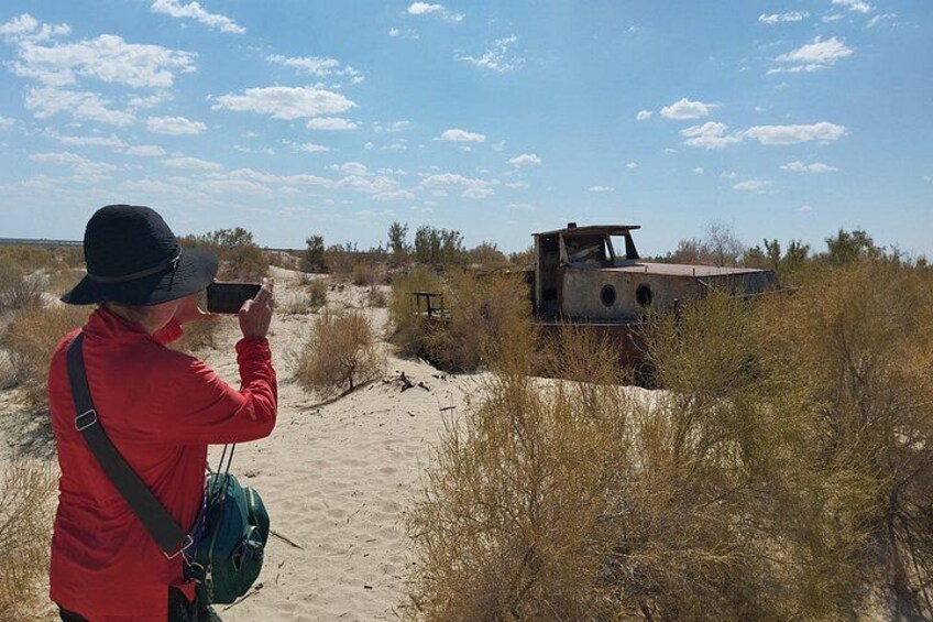 A person in a red jacket taking a photo of a rusted train car in a desert landscape. 5