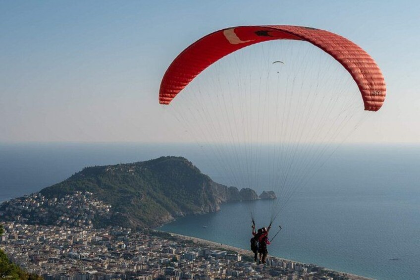 A person paragliding over a coastal city with a red parachute, a mountain, and the sea in the background. 2