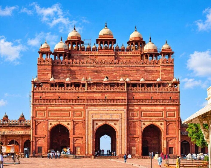 A large red sandstone gateway with multiple domes and arches, surrounded by a clear blue sky. 2